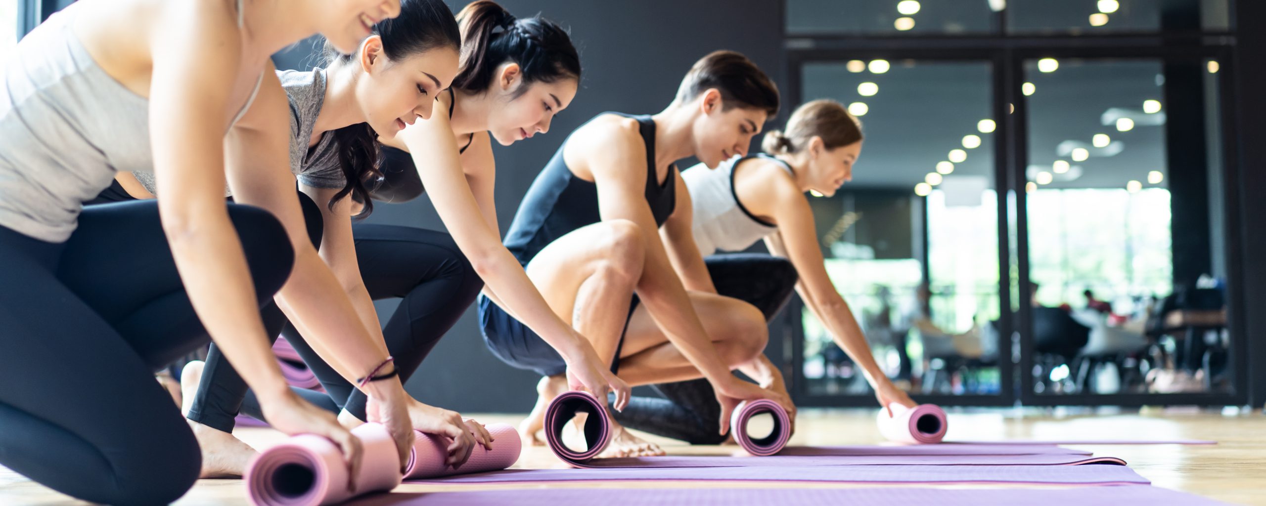 Group of sporty diversity people rolling the yoga mat after training yoga workout in studio room at gym fitness club. They have a good body shape and fit due to exercise and training yoga. Banner size